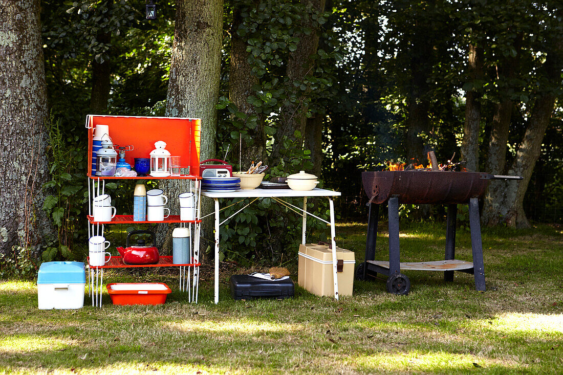 Beleuchteter Grill und Kühlbox mit Klappregalen und Haushaltswaren im Garten des Bauernhauses von Brabourne, Kent, Großbritannien