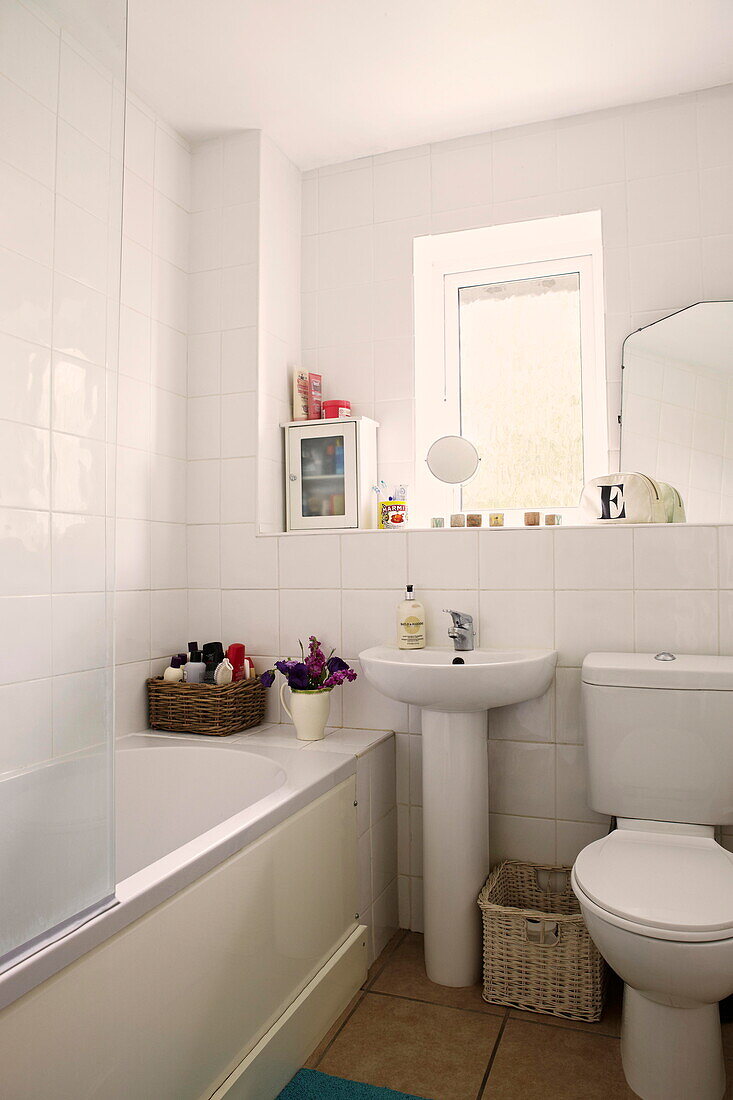 Wicker baskets in white tiled bathroom of Birmingham home  England  UK