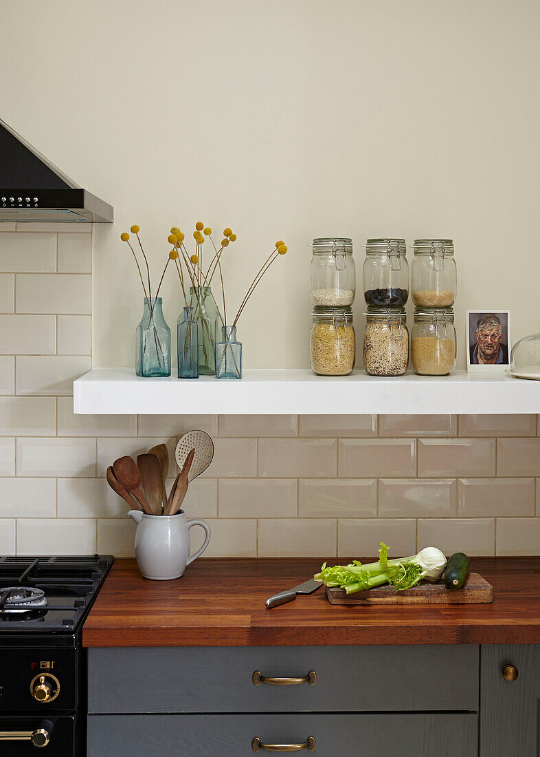 Storage jars and wooden spoons with vegetables on wooden worktop in contemporary London kitchen   England   UK