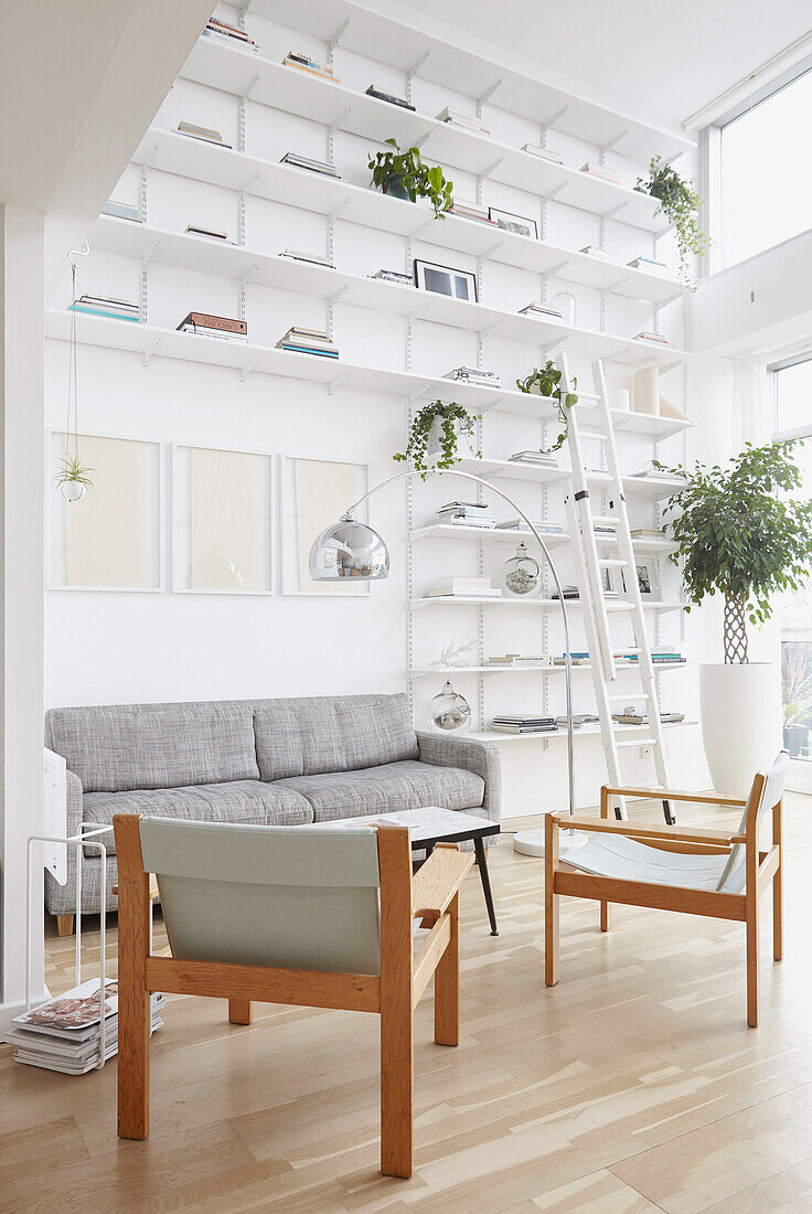 Pair of armchairs in double height living room with floor to ceiling shelving  London home  UK