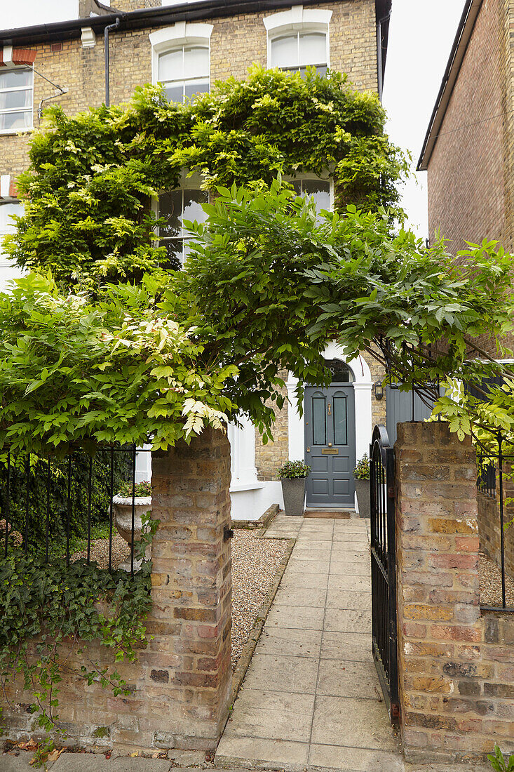 Blick durch ein überwuchertes Tor mit gepflastertem Weg zur Haustür eines Hauses in London England UK