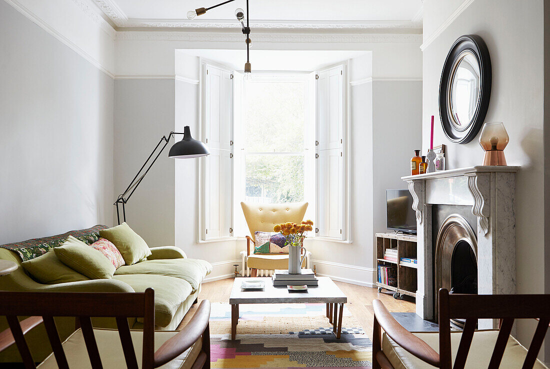 Circular mirror above marble fireplace with vintage furniture in London home  UK