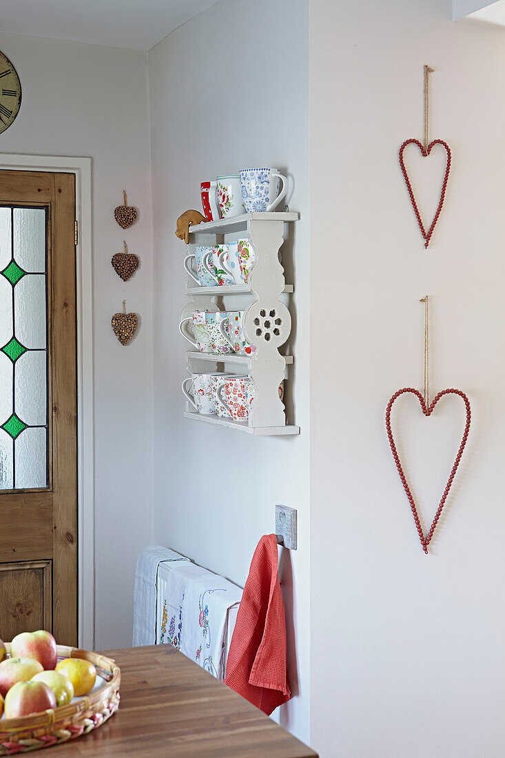 Collection of cups on wall-mounted shelf unit with beaded hearts in Bolton home,  Greater Manchester,  England,  UK
