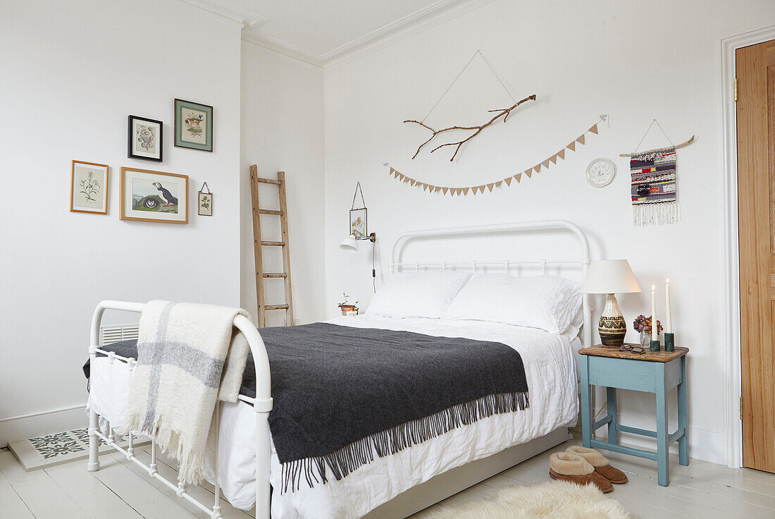 Slippers and table beside bed with grey blanket in London home  UK