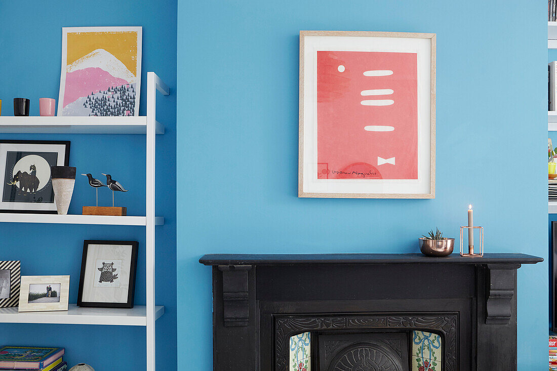 Artwork and ornaments on shelving with Victorian fireplace and bright blue wall in Sheffield home  Yorkshire  UK