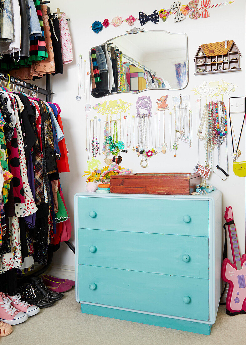 Bunte Vintage-Kleider und Halsketten hängen neben einer bemalten Kommode im Ankleidezimmer eines Hauses in York, England UK