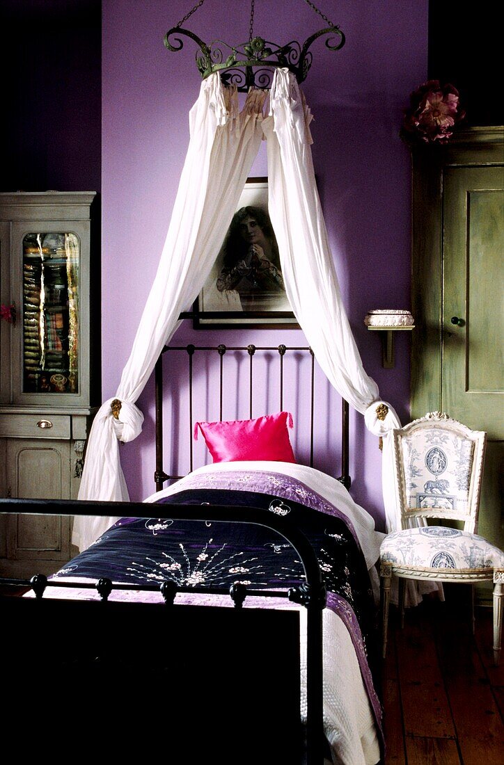 Girl's lilac bedroom with cast iron single bed and metal chandelier with muslin drapes