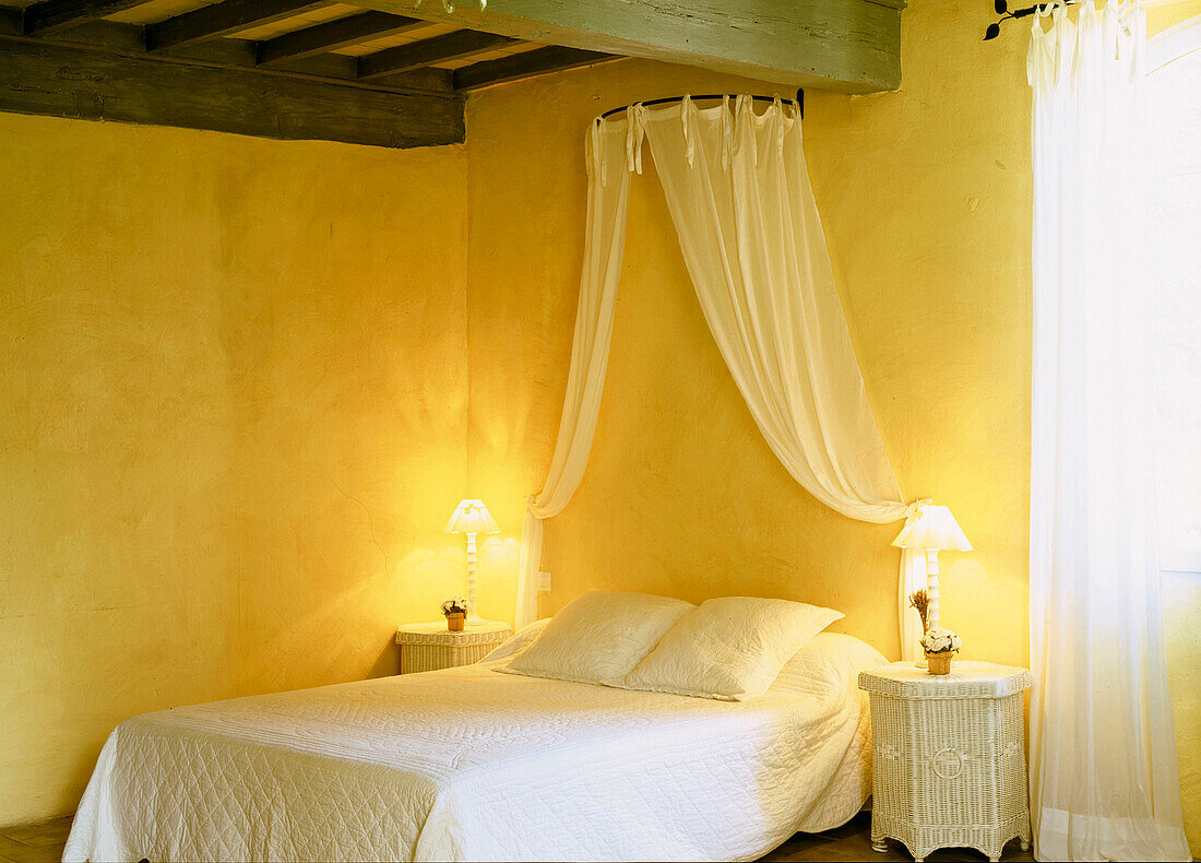 Sunny yellow double bedroom with bedside lights and canopy of drapes