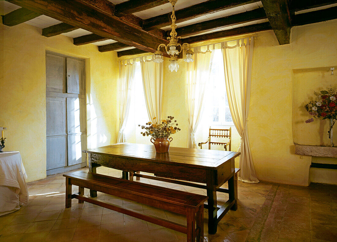 Traditional French dining room with antique refectory table and benches on a tiled stone floor