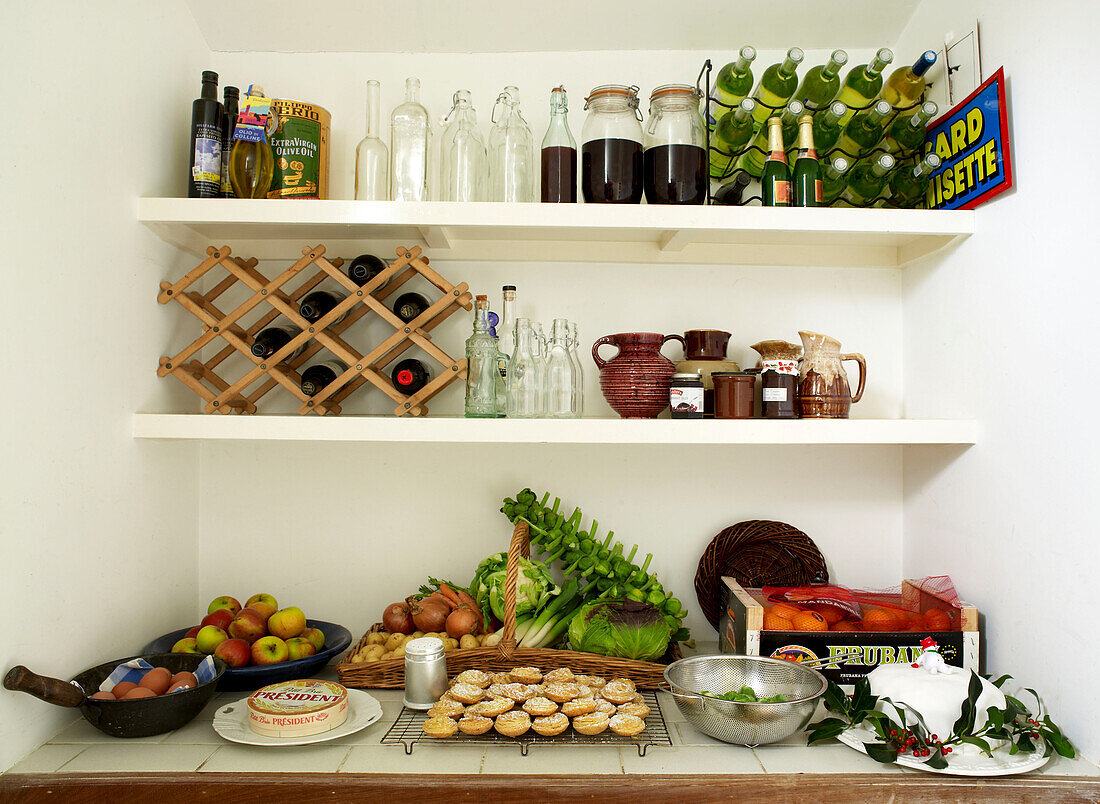 Close up of pantry filled with wine bottles mince pies fruit and vegetables and a christmas cake
