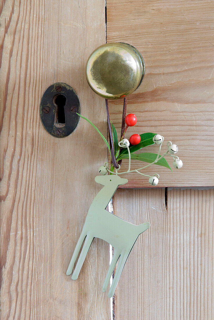 Türknauf und Schlüsselloch aus Messing an einer Tür aus gestrichenem Kiefernholz mit hängendem Rentier-Weihnachtsschmuck