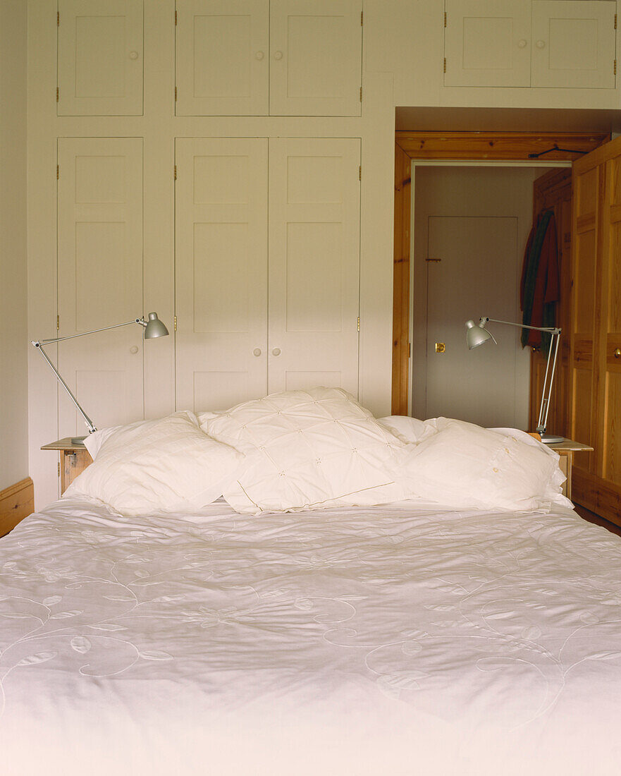 Bed with white linen and lamps fitted wardrobes and open door