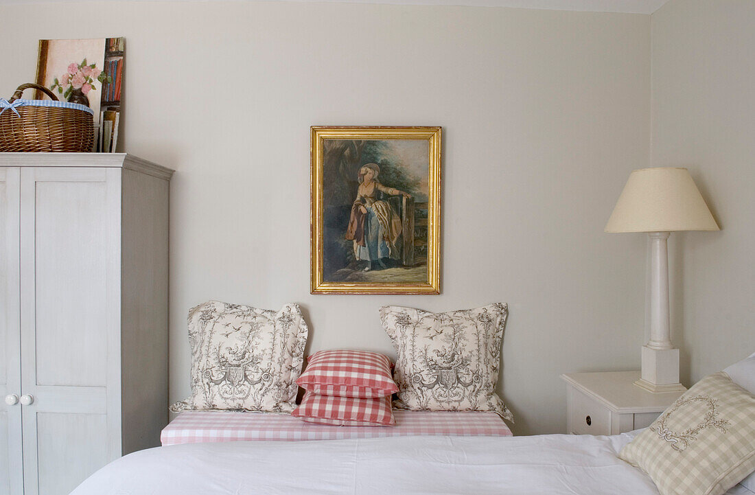 Artwork above ottoman covered in a pink and white check with toile and checked cushions 