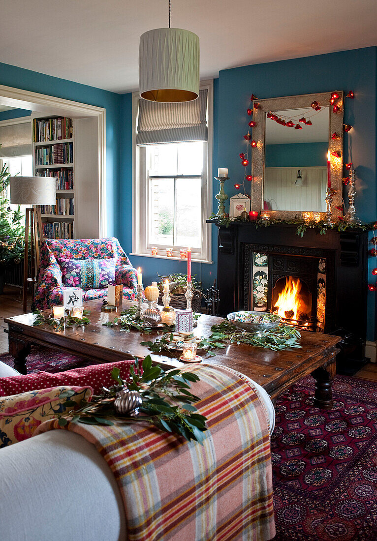 Beleuchtetes Feuer und Lichterketten mit hölzernem Couchtisch in einem Landhaus zu Weihnachten