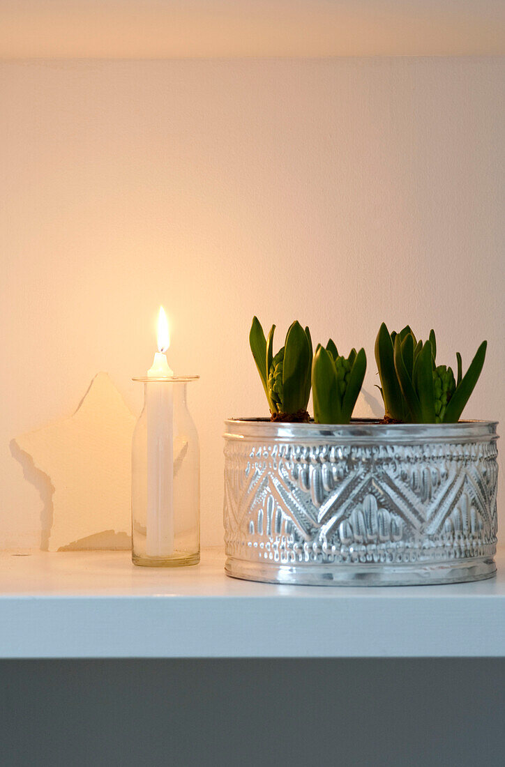 Christmas ornaments and eucalyptus with a crocuses and lit candles on shelving 