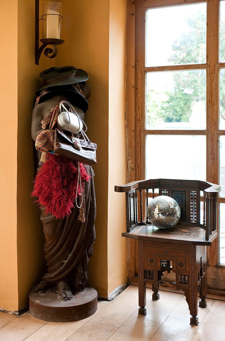 Hüte und Taschen auf weiblicher Statue mit antikem Stuhl und Discokugel im Eingang eines Hauses in Großbritannien