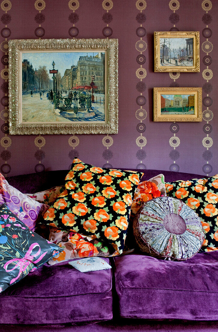 Verschiedene bunte Kissen auf einem lila Sofa unter einem Kunstwerk in einem Londoner Haus (UK)