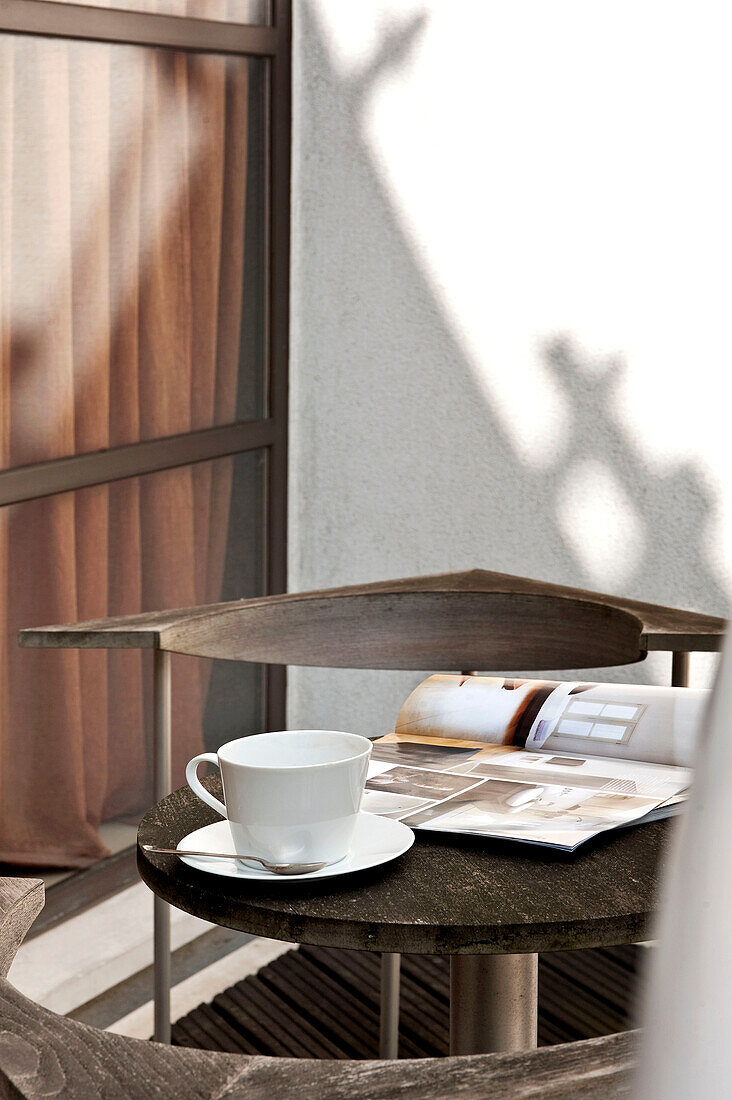 Tasse und Untertasse mit aufgeschlagener Zeitschrift auf dem Tisch einer Balkonaußenwohnung in London England UK