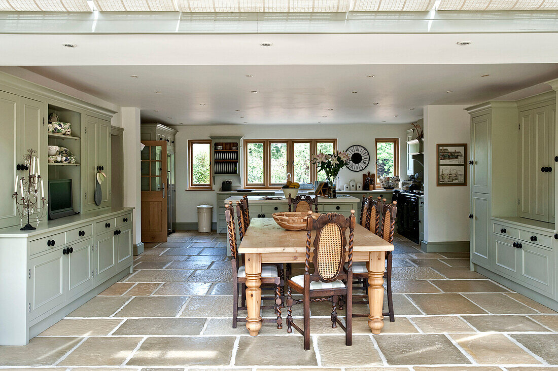Wooden dining table and chairs in spacious open plan flagstone kitchen of Canterbury home England UK