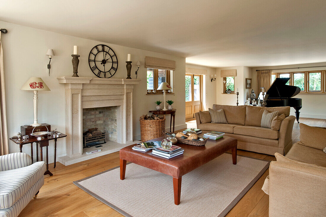 Grand piano in drawing room with leather ottoman in front of fireplace with antique roman clock in Canterbury home England UK