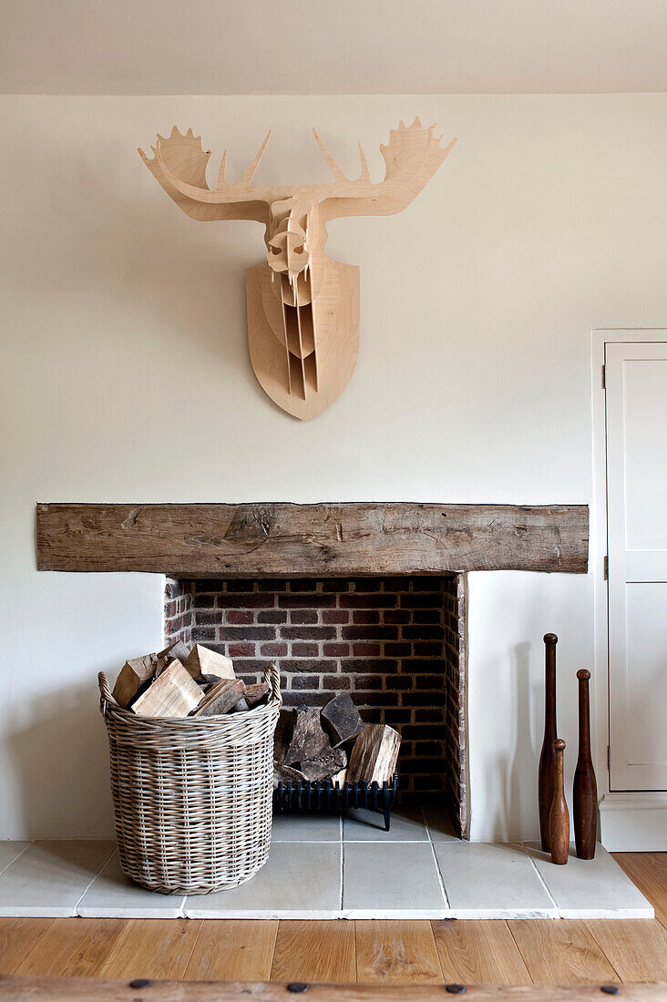 Carved wooden stags head mounted above exposed brick fireplace with log basket in Canterbury home England UK