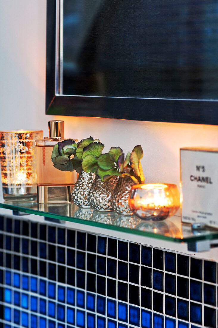 Perfume bottles and cut leaves on glass shelf in bathroom of Forest Row family home, Sussex, England, UK