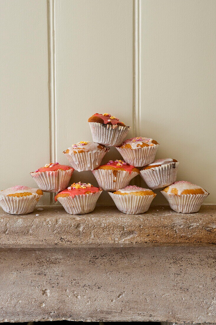 Selbstgemachte Cupcakes auf einem steinernen Kaminsims mit einer gelb getäfelten Wand in einem Haus in Buckinghamshire, England, UK