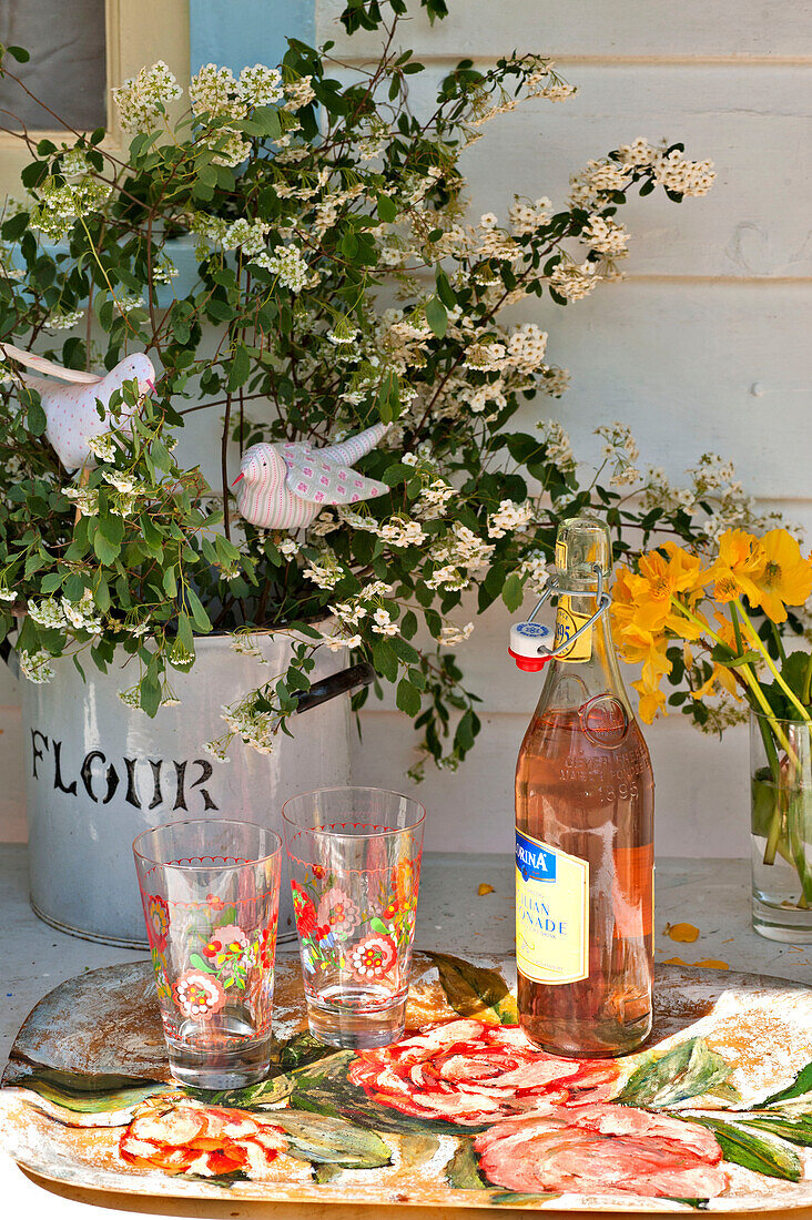 Pink lemonade and glasses with cut flowers on table in sunlight, Essex home, England, UK