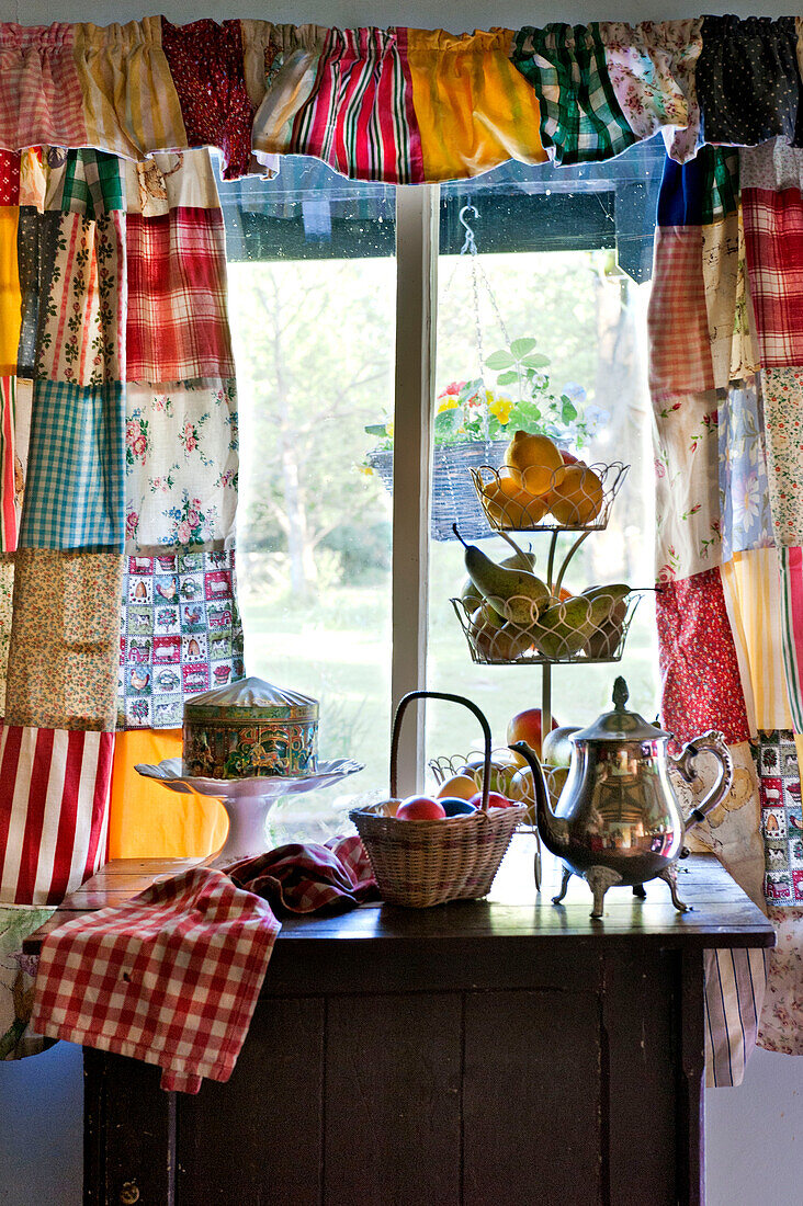 Silberne Teekanne mit Früchten auf Beistelltisch mit Patchworkvorhängen in einem Haus in Essex, England, Vereinigtes Königreich