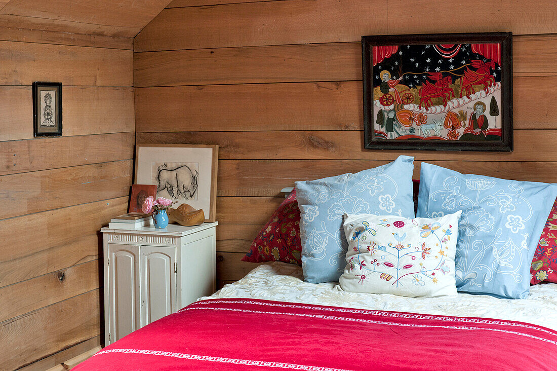 Embroidered cushions on bed in wood clad room of Essex home, England, UK