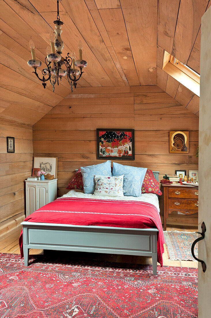 Double bed with red blanket in wood clad room with vintage light fitting, Essex home, England, UK