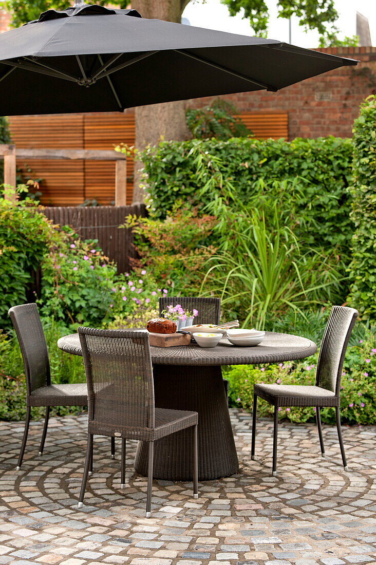 Tisch und Stühle mit Sonnenschirm auf dem Innenhof eines Hauses in Middlesex, London, England, Vereinigtes Königreich
