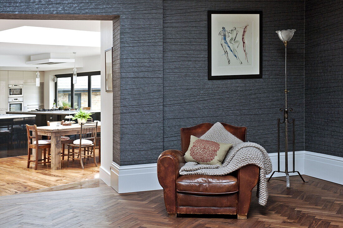 Brauner Ledersessel im Wohnzimmer mit Parkettboden und Blick in die Küche in einem Haus in London, England, Vereinigtes Königreich