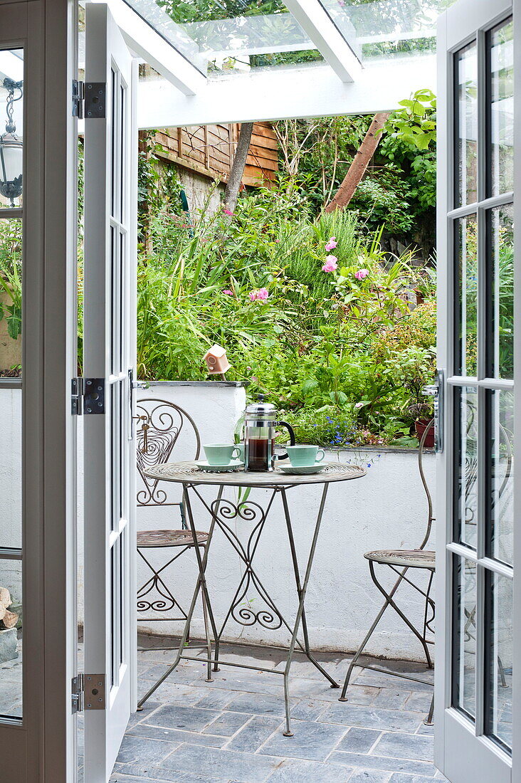 Coffee pot and cups on metal table with chairs on patio of Padstow cottage, Cornwall, England, UK