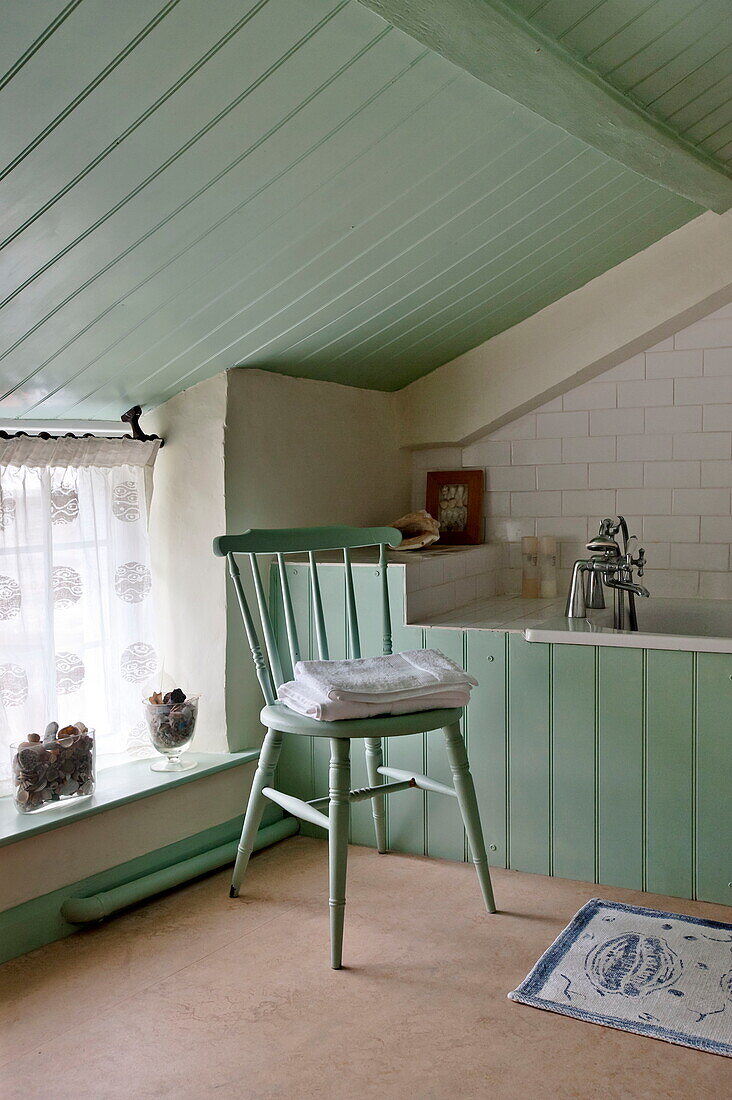 Folded towels on chair in green painted attic bathroom, Padstow cottage, Cornwall, England, UK