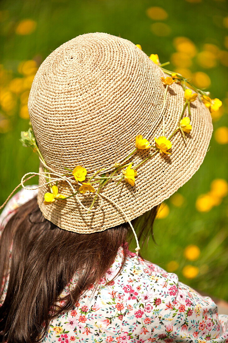 Frau sitzend mit Hahnenfußkette (Ranunculus) Hut in Brecon, Powys, Wales, UK