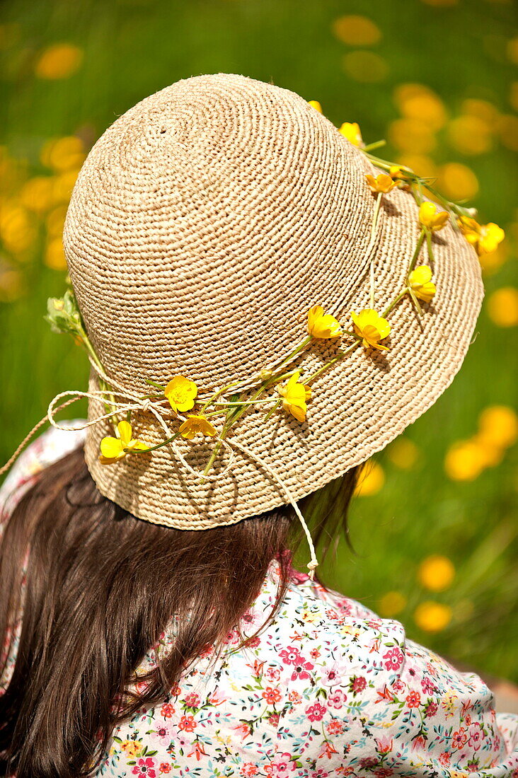 Woman sitting with buttercup chain (Ranunculus) hat in Brecon, Powys, Wales, UK