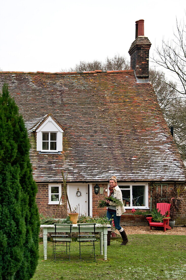 Woman walking in garden of Shropshire tiled cottage, England, UK
