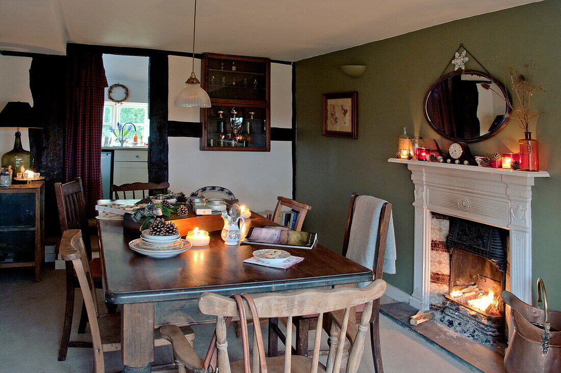 Esstisch und Stühle aus Holz mit beleuchtetem Feuer in einem Cottage in Shropshire, England, UK