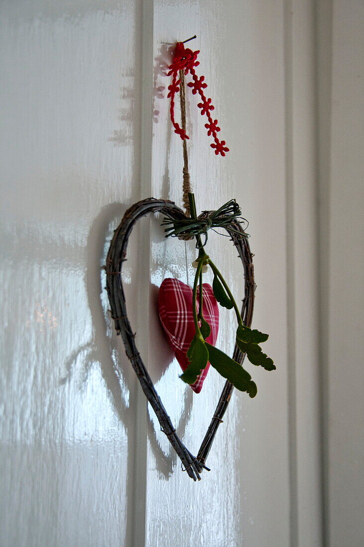 Heart shaped ornament with mistletoe on white panelled door in Shropshire cottage, England, UK