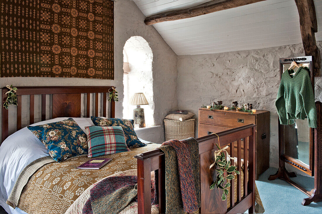 Gold and red wall hanging above wooden bed in whitewashed bedroom of Tregaron home Wales UK