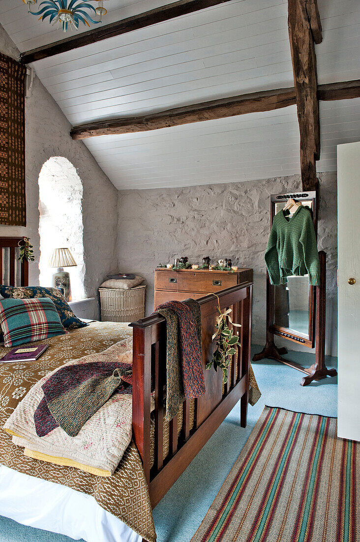 Striped rug at foot of wooden bed in whitewashed bedroom of Tregaron home Wales UK