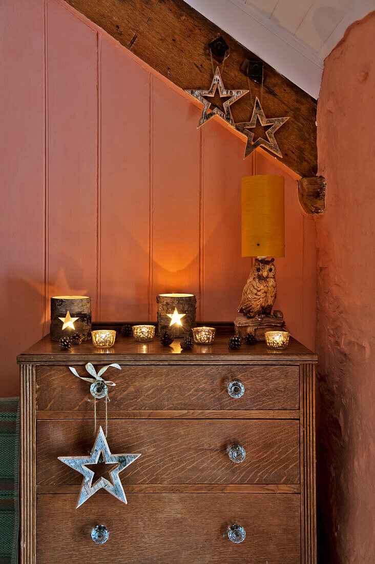 Holzkommode mit sternförmigen Dekorationen und Kerzenhaltern im pfirsichfarbenen Schlafzimmer eines Hauses in Tregaron, Wales, UK