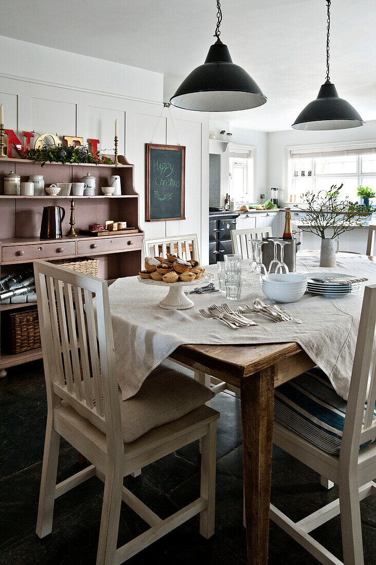 Schwarze Pendelleuchte über einem Tisch mit weiß gestrichenen Stühlen in einem Esszimmer in Crantock, Cornwall, England, UK