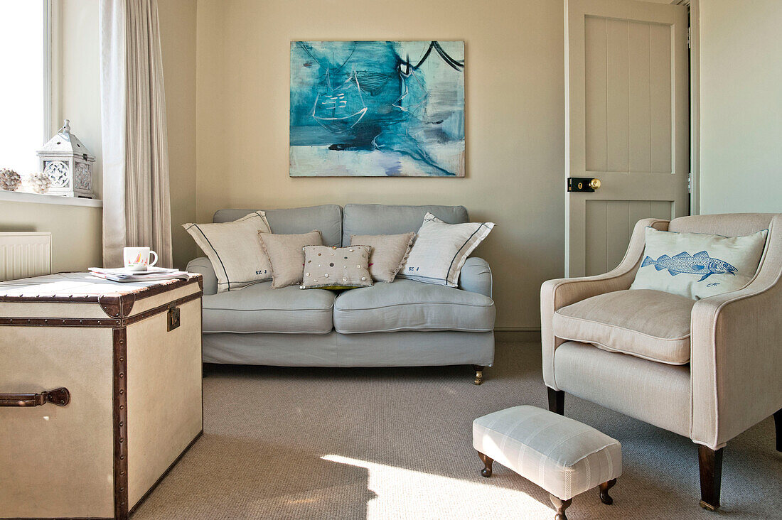 Cremesessel mit hellgrauem Sofa und modernem Kunstwerk im Wohnzimmer eines Einfamilienhauses Cornwall UK