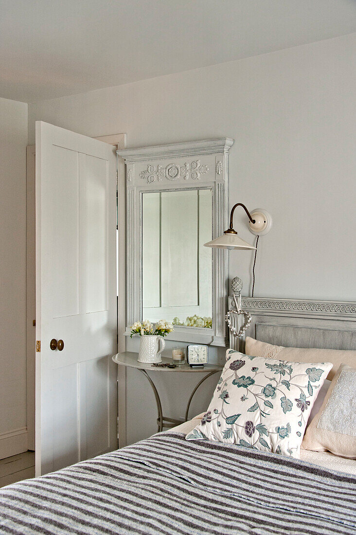 Floral print cushion on bed with mirror and lamp in Crantock home Cornwall England UK