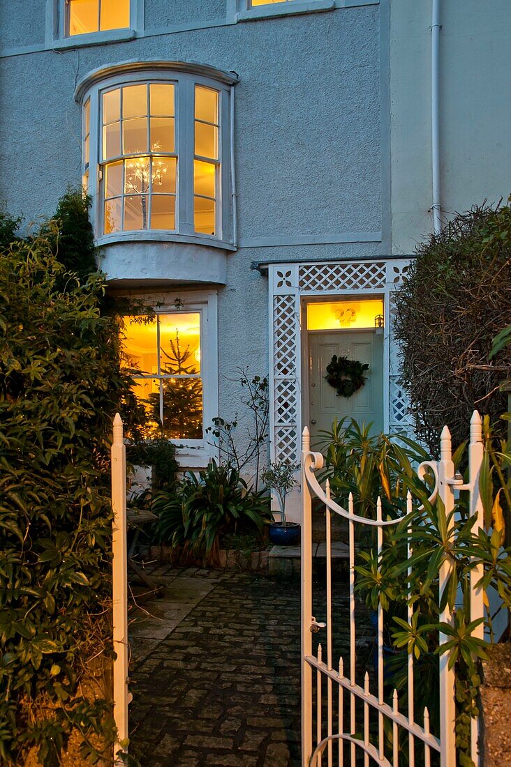 Open gate and lit windows of pebble-dashed Penzance terraced house Cornwall England UK