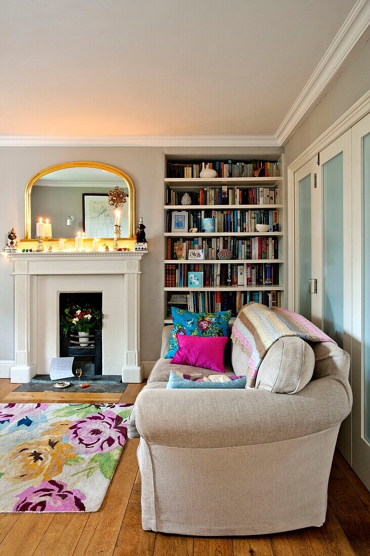 Lit candles on mantlepiece in living room with bookcase and sofa in Penzance family home Cornwall England UK