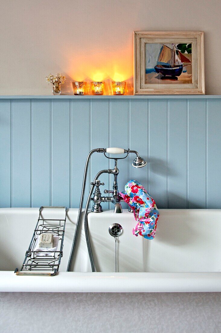 Beleuchtete Teelichter über einer hellblau getäfelten Badewanne mit Duscharmatur und Ablage in einem Einfamilienhaus in Penzance, Cornwall, England UK