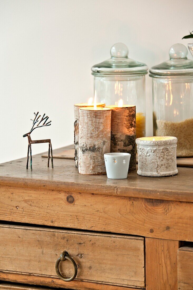 Storage jars and lit candles with metal reindeer on wooden sideboard in Wadebridge home, North Cornwall, UK